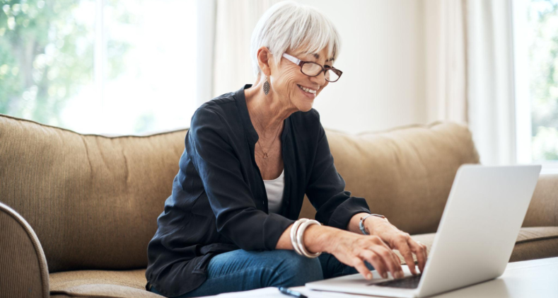 A senior woman smiles as she searches for CD rates on the computer in her living room